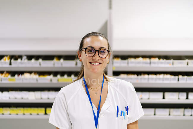 Усмішка жінки - фармацевта стоїть навпроти лікарських полиць у коморі. — стокове фото
