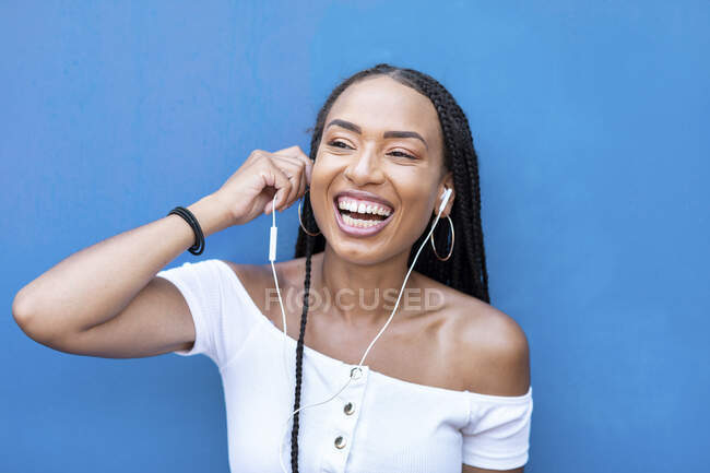 Mulher alegre ouvindo música enquanto está de pé contra a parede azul — Fotografia de Stock