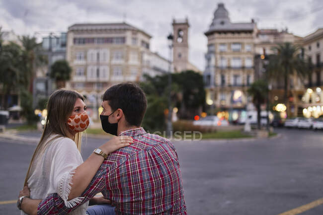 Casal usando máscara protetora sentado na rua na cidade — Fotografia de Stock