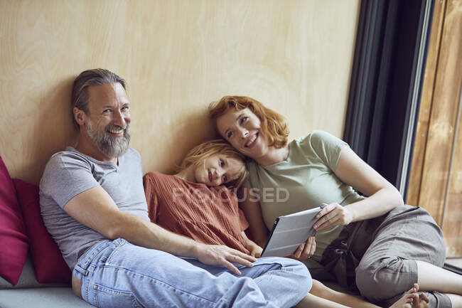 Pais sorridentes com a filha usando tablet digital enquanto deitado na cama em casa — Fotografia de Stock