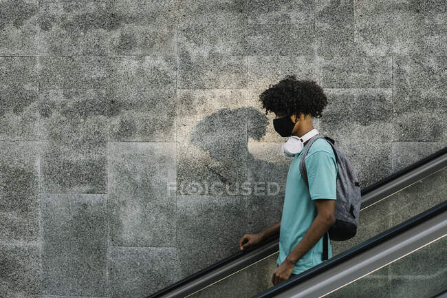 Hombre con máscara protectora de pie en la pared de escaleras mecánicas en la ciudad - foto de stock