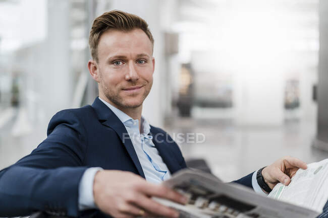 Усміхнений бізнесмен читає газету, сидячи в місті — стокове фото
