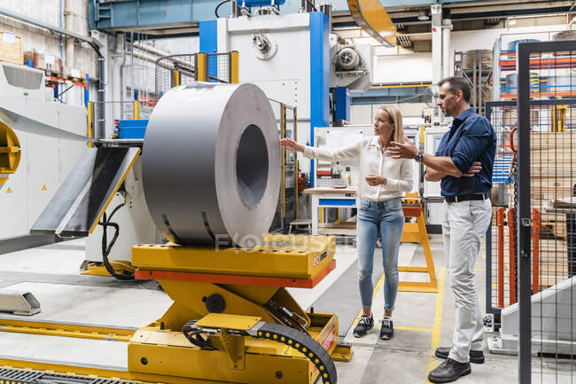 Female entrepreneur examining steel roll with male colleague while standing in factory — Stock Photo
