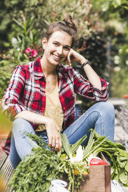 Souriant belle femme avec des légumes assis dans le jardin communautaire — Photo de stock