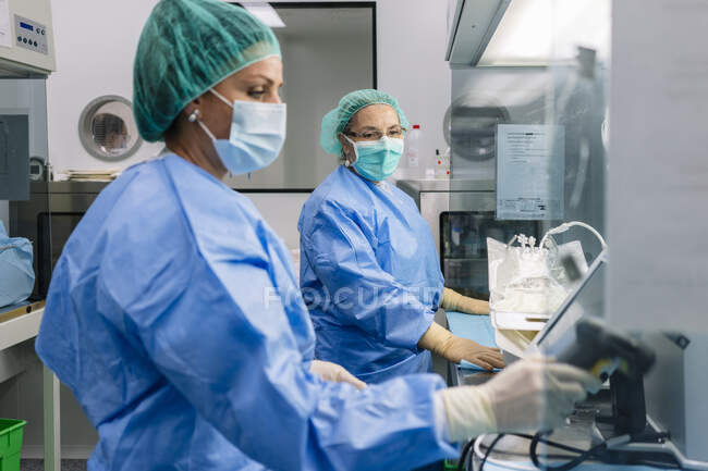 Аптекарь смотрит на коллегу, держащую сканер штрих-кода в лаборатории — стоковое фото