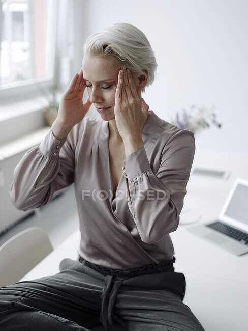 Empresária com cabeça nas mãos meditando sentado na mesa no escritório do loft — Fotografia de Stock