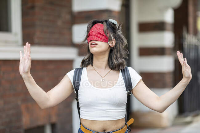 Young woman wearing red face mask on eye gesturing while standing in city — Photo de stock