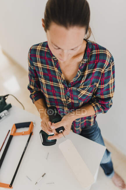 Woman changing drill bit of electric drill while standing at home — Stock Photo