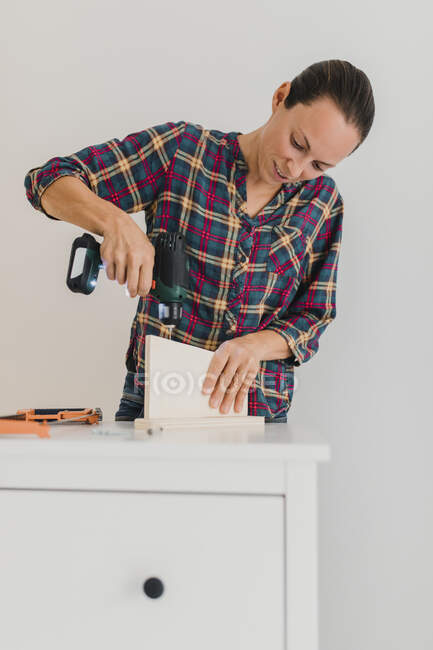 Mitte erwachsene Frau benutzt Elektrobohrmaschine, während sie zu Hause am Schrank arbeitet — Stockfoto