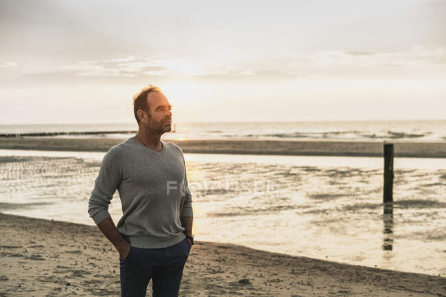 Thoughtful man with hands in pockets standing against sea during sunset — Foto stock