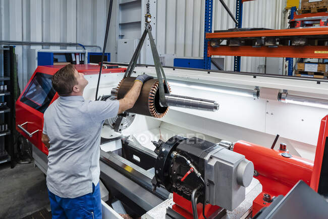 Mature male manual worker looking at machine part hanged up on hook at industrial factory — Stock Photo