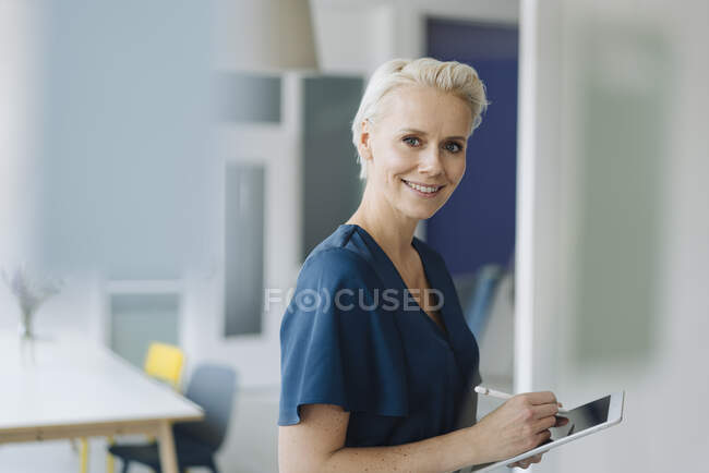 Empreendedora sorridente trabalhando sobre tablet digital enquanto estava no escritório — Fotografia de Stock