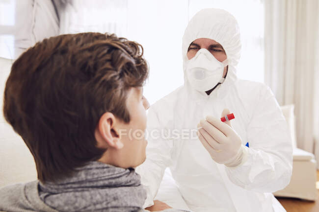 Arzt im Schutzanzug macht Coronavirus-Test bei jungem Mann zu Hause — Stockfoto