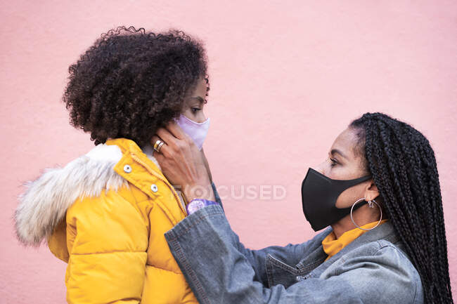 Madre regolazione maschera viso della figlia contro muro rosa — Foto stock