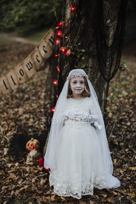 Petite fille debout tout en portant costume de mariée cadavre contre arbre dans la forêt — Photo de stock