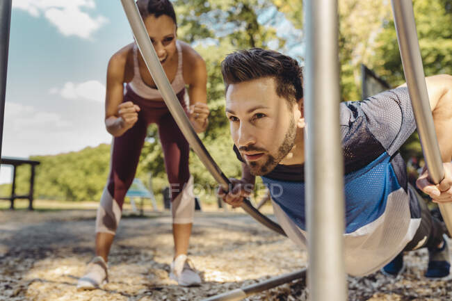 Frau unterstützt Mann bei Liegestützen auf Fitnessparcours — Stockfoto