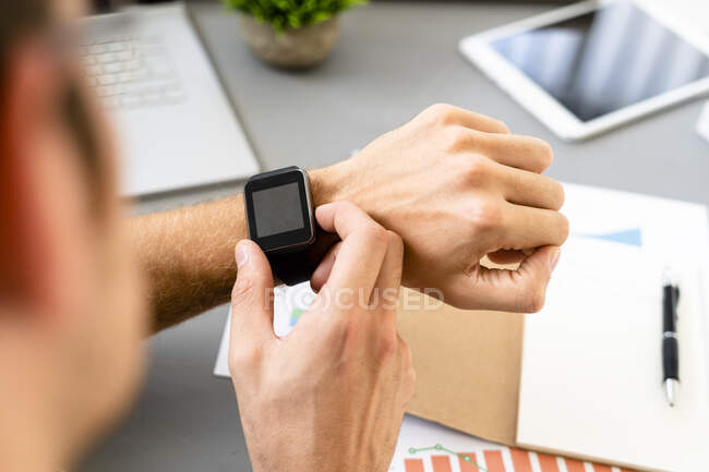Homme regardant la montre intelligente assis près du bureau au bureau — Photo de stock