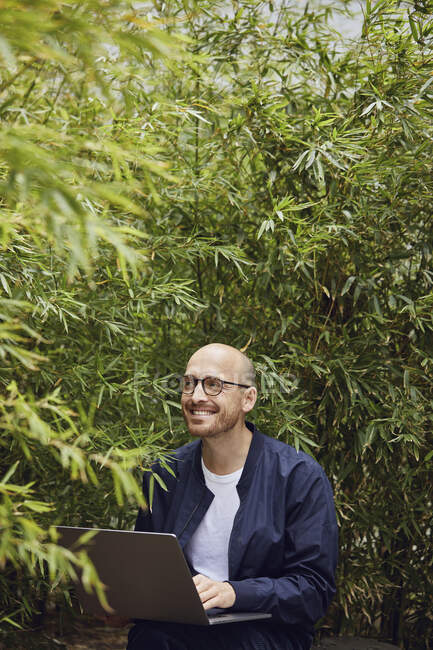 Sorrindo homem sentado ao usar laptop no parque público — Fotografia de Stock