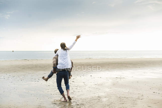 Зрілий чоловік свинарство весела жінка під час прогулянки на пляжі під час заходу сонця — стокове фото