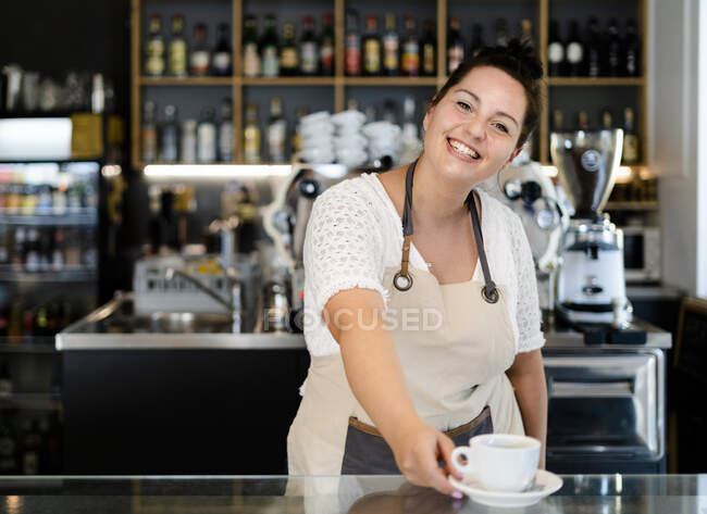 Smiling female owner serving coffee cup on bar counter while working in cafe — Stock Photo