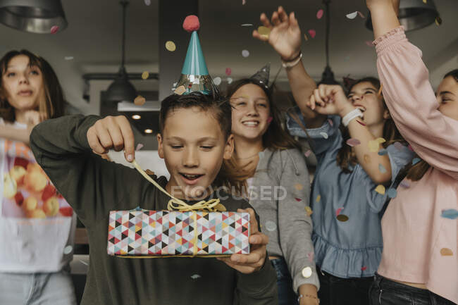 Curieux cadeau d'ouverture de garçon d'anniversaire tandis que les amis dansent en arrière-plan — Photo de stock
