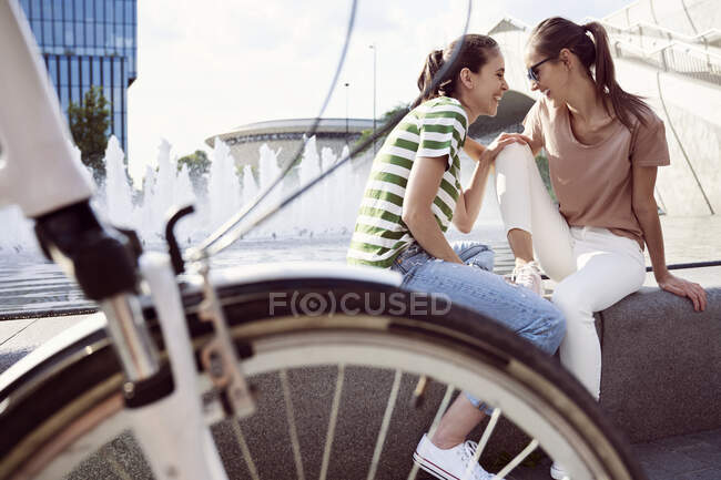 Amici allegri seduti sul muro di contenimento mentre trascorrono il fine settimana insieme in città — Foto stock