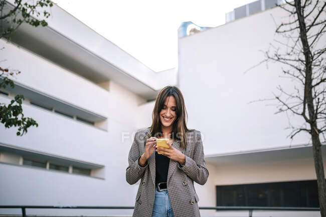 Lächelnde Frau per SMS auf dem Smartphone, während sie vor dem Gebäude steht — Stockfoto