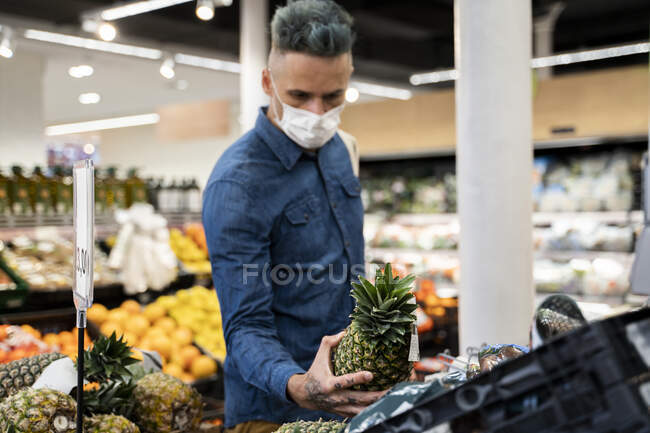 Mid adult man wearing face mask buying pineapple in supermarket — Stock Photo