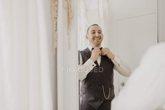 Жених регулирует лук, глядя в зеркало в магазине свадебных платьев — стоковое фото