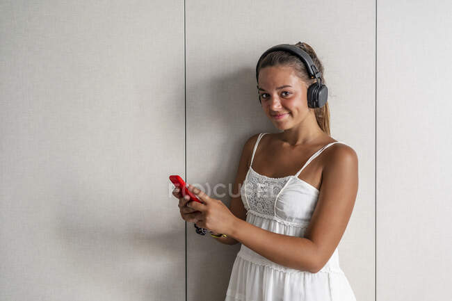Smiling woman with smart phone standing against closet at home — Stock Photo