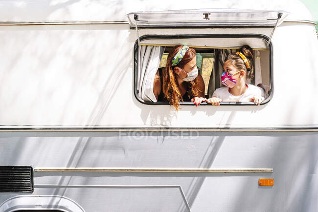 Mutter und Tochter mit Masken schauen sich im Wohnmobil durch Fenster an — Stockfoto