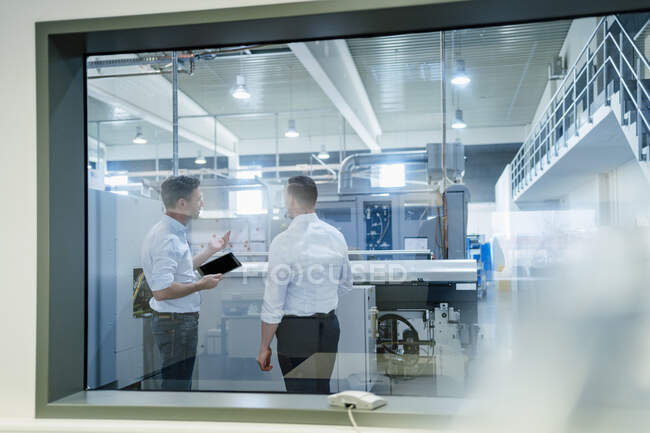 Collèges masculins avec tablette numérique discutant de machines en usine — Photo de stock