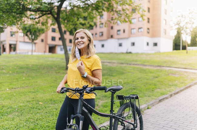 Donna sorridente in piedi con la bicicletta sul sentiero in città durante COVID-19 — Foto stock
