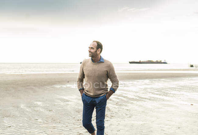 Mature man with hands in pockets contemplating while standing against sea during sunset - foto de stock