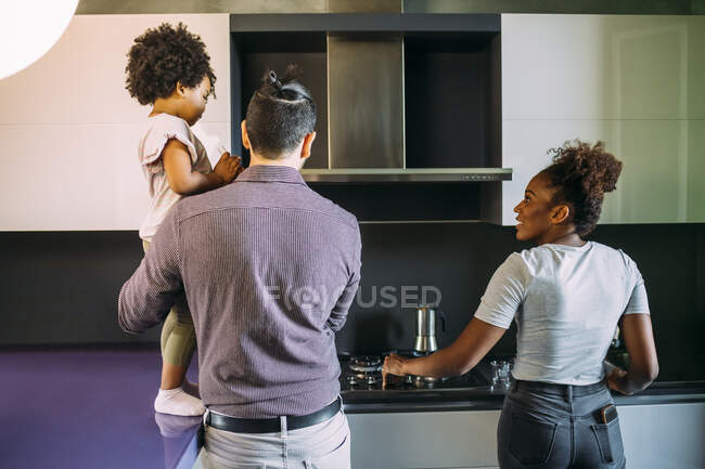 Чоловік, який носить доньку стоячи з жінкою, готує каву на плиті на кухні. — стокове фото