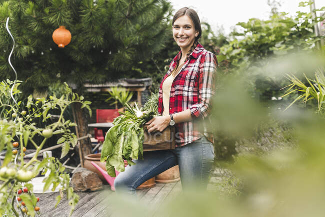 Smiling young woman carrying crate while standing in vegetable garden — Foto stock