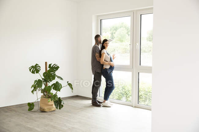 Femme enceinte debout avec mari regardant par la fenêtre dans une nouvelle maison — Photo de stock