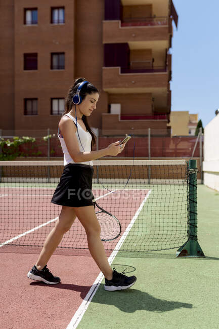 Теннисистка в наушниках с помощью смартфона во время прогулки по корту — стоковое фото