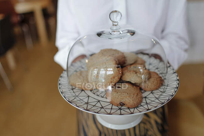 Close-up of female owner holding cookies in plate with cloche at coffee shop — Stock Photo