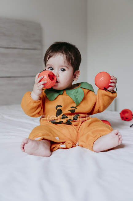 Bonito criança do sexo masculino brincando com abóbora halloween brinquedo enquanto sentado na cama em casa — Fotografia de Stock