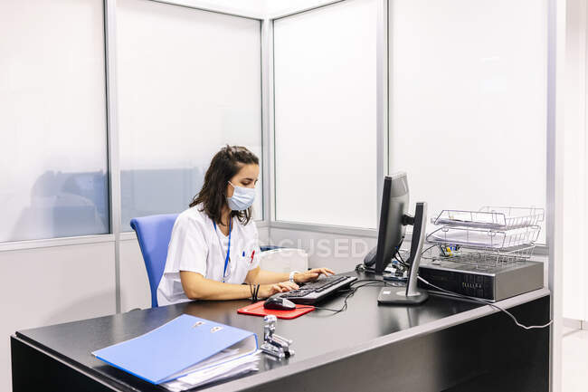 Médica mulher usando máscara cirúrgica usando computador na mesa no escritório no hospital — Fotografia de Stock