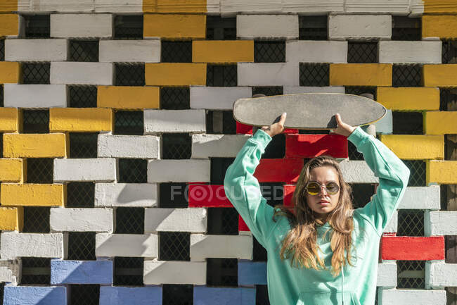 Junge Frau hebt Skateboard, während sie gegen Mauer steht — Stockfoto