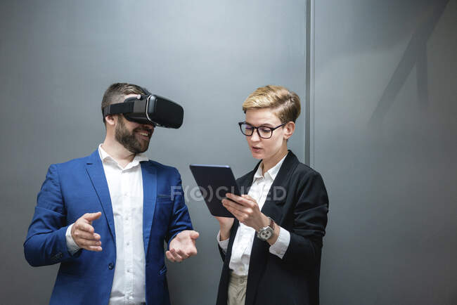 Female entrepreneur using digital tablet while analyzing colleague experiencing virtual reality simulation at office — Photo de stock