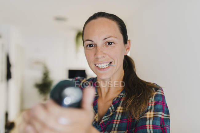 Mitte erwachsene Frau hält Schraube im Mund, während sie zu Hause mit Elektroschrauber arbeitet — Stockfoto