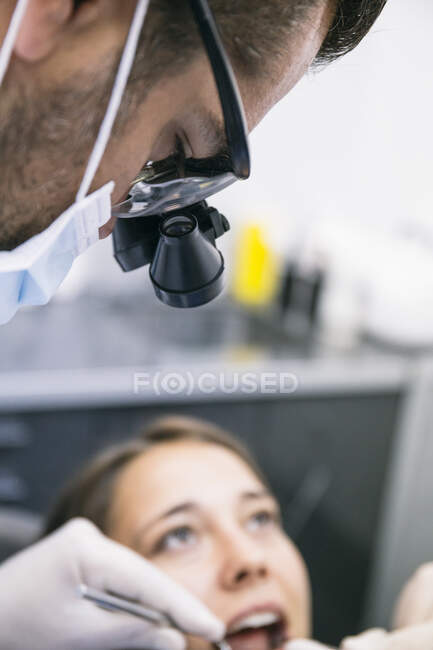 Dentista masculino em lupas cirúrgicas examinando dentes de paciente feminino na clínica — Fotografia de Stock