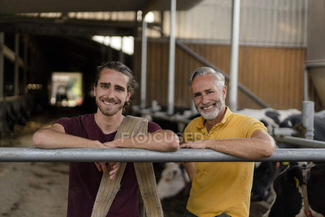 Портрет улыбающегося взрослого фермера со взрослым сыном в коровнике на ферме — стоковое фото