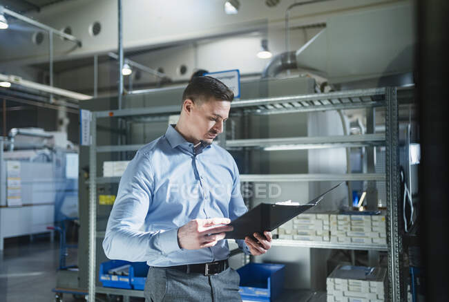 Male professional looking at file in factory by rack — Stock Photo