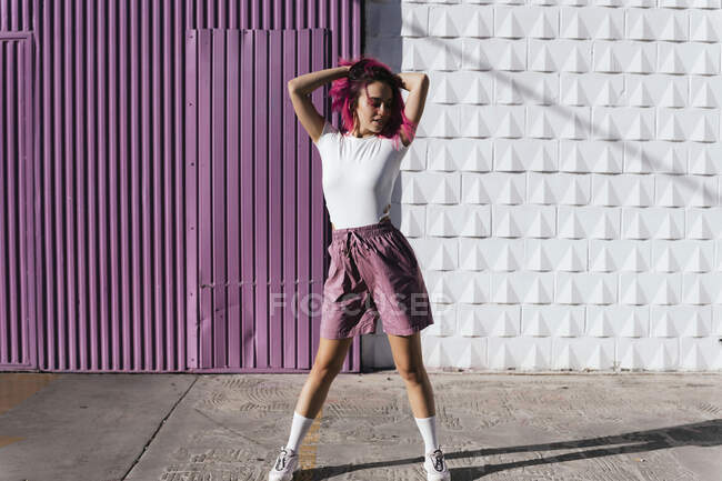 Mujer joven con el pelo rojo teñido bailando delante de la pared púrpura en la ciudad - foto de stock