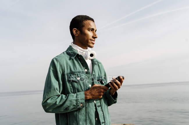 Giovane con smart phone in piedi contro il mare — Foto stock