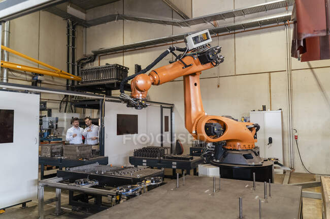 Geschäftsleute stehen in der Fabrik vor Roboterarmautomaten — Stockfoto